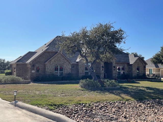 A single-story stone house with a front yard, small tree, and rock landscaping, under a clear blue sky.